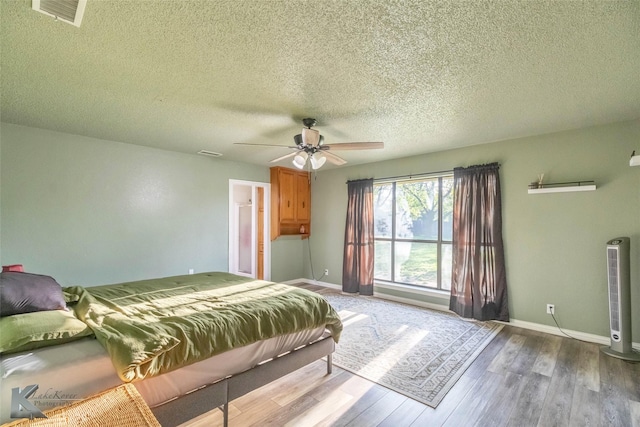 bedroom featuring baseboards, wood finished floors, visible vents, and a textured ceiling