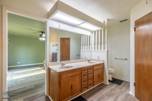 bathroom featuring wood finished floors, a sink, a textured ceiling, double vanity, and toilet