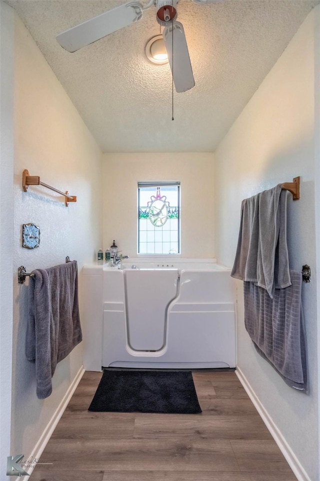 full bathroom featuring a bath, baseboards, wood finished floors, and a textured ceiling