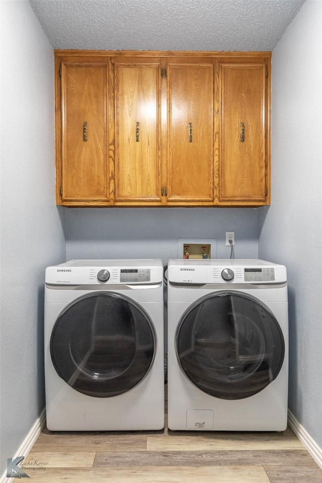laundry room with a textured ceiling, washer and dryer, cabinet space, light wood-style flooring, and baseboards