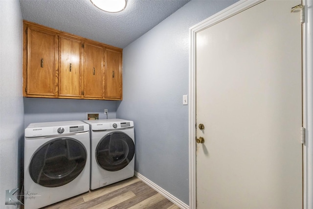 washroom featuring a textured ceiling, washing machine and dryer, baseboards, light wood-style floors, and cabinet space
