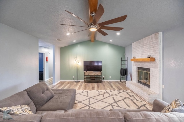 living area with vaulted ceiling, wood finished floors, visible vents, a ceiling fan, and a brick fireplace