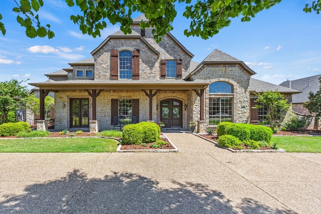 french country inspired facade with stone siding, a porch, and french doors