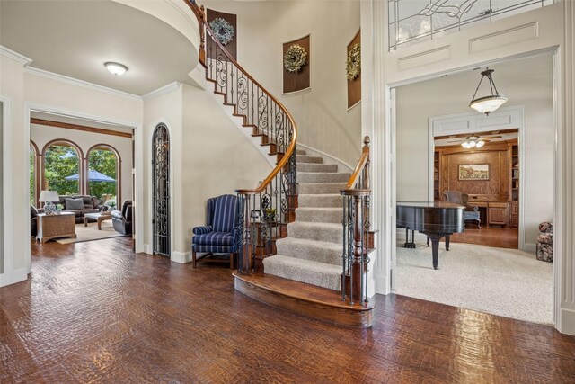 foyer entrance with stairway, a towering ceiling, wood finished floors, ornamental molding, and baseboards