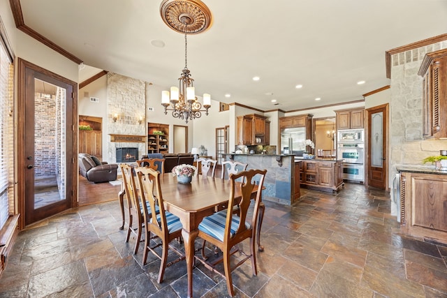 dining area featuring a fireplace, stone tile flooring, and ornamental molding
