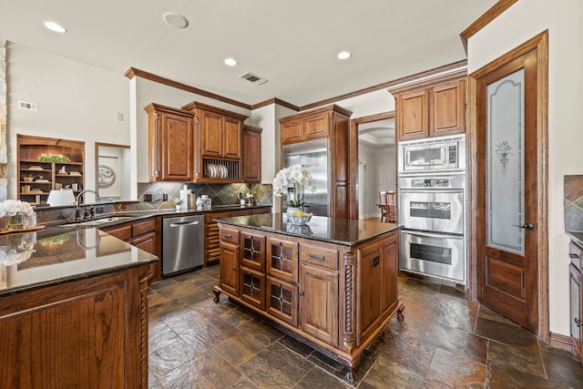 kitchen with a sink, built in appliances, stone tile flooring, ornamental molding, and visible vents