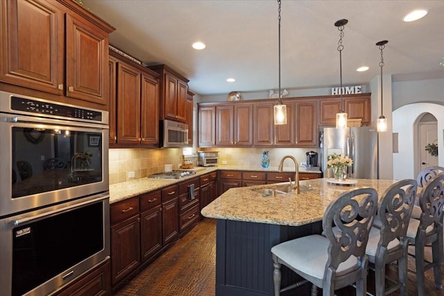 kitchen with a kitchen breakfast bar, light stone counters, stainless steel appliances, a sink, and arched walkways