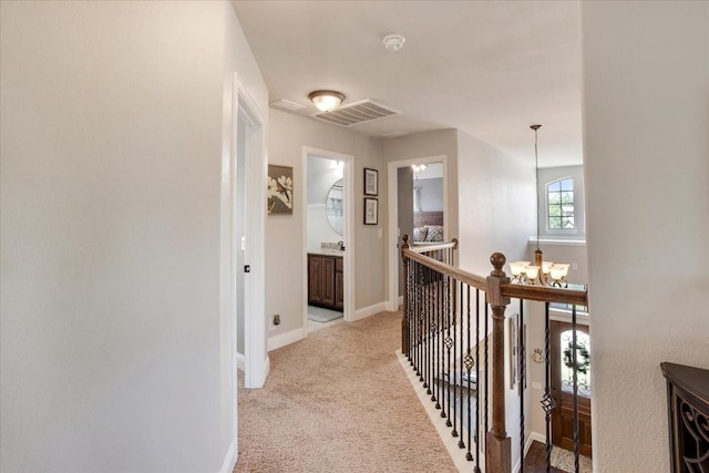 corridor with baseboards, visible vents, a notable chandelier, an upstairs landing, and light colored carpet