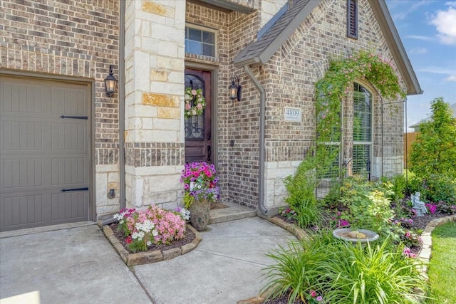 view of exterior entry featuring concrete driveway, brick siding, stone siding, and a garage