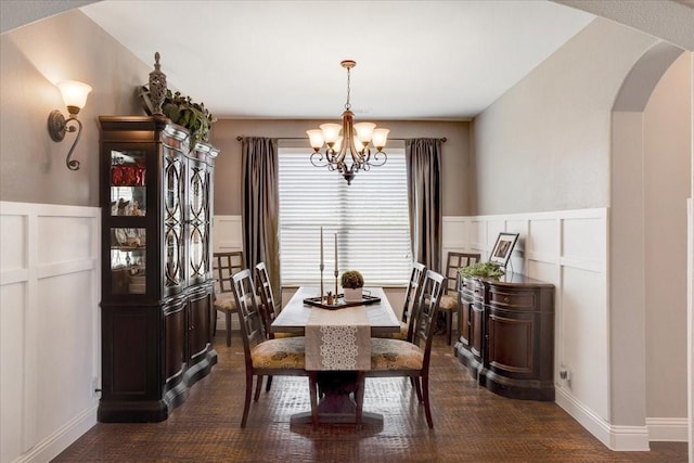 dining room with a wainscoted wall, arched walkways, a notable chandelier, and a decorative wall