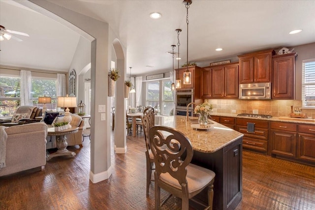 kitchen featuring open floor plan, a breakfast bar, arched walkways, stainless steel appliances, and light stone countertops