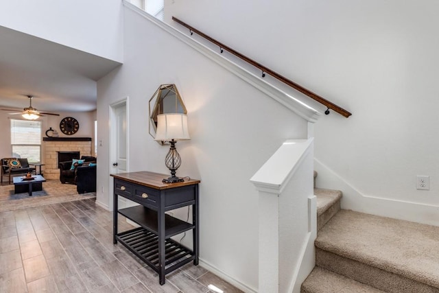 stairway with ceiling fan, baseboards, wood finished floors, and a stone fireplace