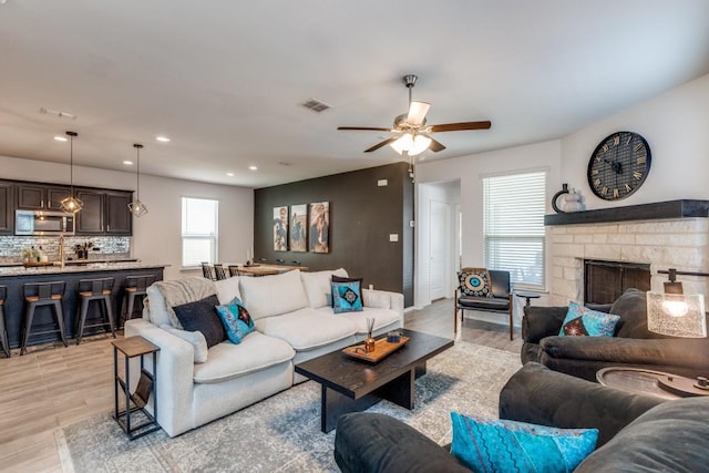 living area featuring a fireplace, a ceiling fan, visible vents, and light wood-type flooring