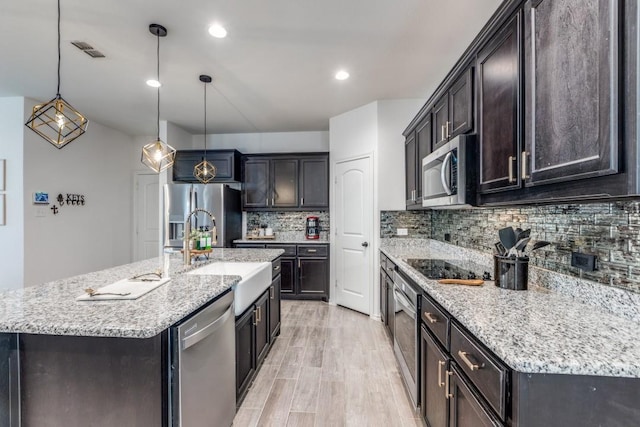 kitchen with light wood finished floors, stainless steel appliances, a sink, visible vents, and backsplash