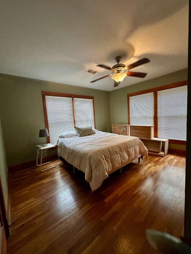 bedroom featuring baseboards, a ceiling fan, wood finished floors, and visible vents