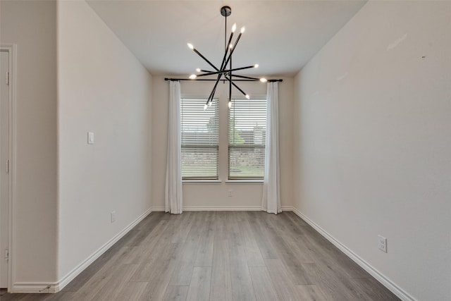 spare room featuring light wood finished floors, baseboards, and a notable chandelier