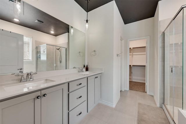 bathroom with a spacious closet, a sink, double vanity, and a stall shower