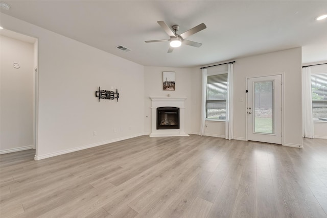 unfurnished living room with a ceiling fan, a glass covered fireplace, light wood-style floors, baseboards, and visible vents