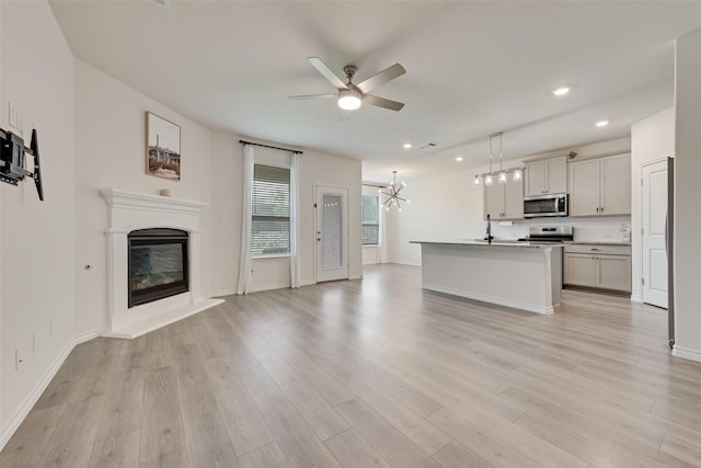 unfurnished living room with a sink, ceiling fan with notable chandelier, a glass covered fireplace, light wood finished floors, and recessed lighting