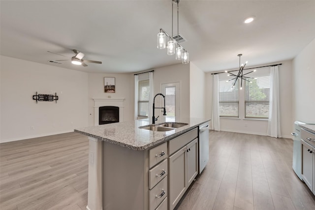 kitchen with dishwasher, a sink, light wood-type flooring, a fireplace, and ceiling fan with notable chandelier