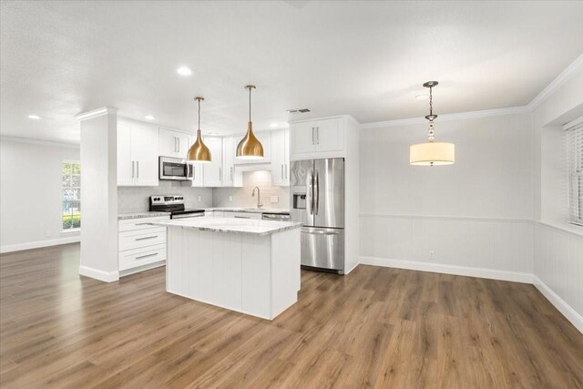 kitchen with a center island, a sink, wood finished floors, crown molding, and appliances with stainless steel finishes