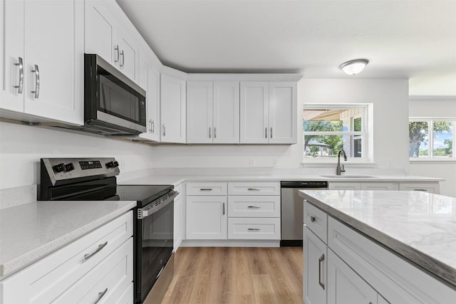 7009 Overhill Rd, Fort Worth, TX 76116 - kitchen featuring white cabinets, light wood finished floors, a sink, light stone countertops, and appliances with stainless steel finishes