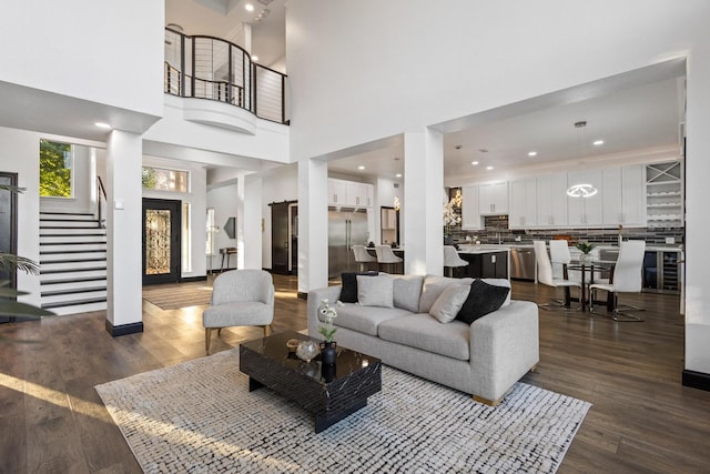 living area with baseboards, a towering ceiling, dark wood-type flooring, and stairway