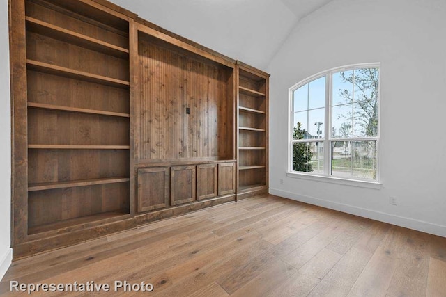 interior space featuring baseboards, lofted ceiling, and light wood finished floors