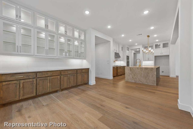 kitchen with white cabinets, a sink, baseboards, glass insert cabinets, and wood finished floors