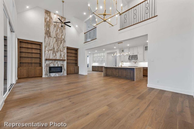 unfurnished living room featuring wood finished floors, ceiling fan with notable chandelier, built in features, a towering ceiling, and a fireplace