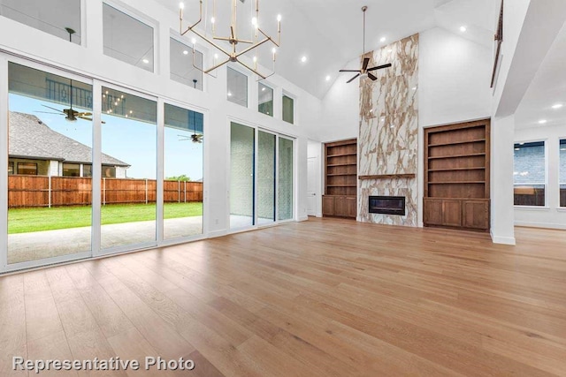 unfurnished living room featuring wood finished floors, built in features, high vaulted ceiling, and ceiling fan