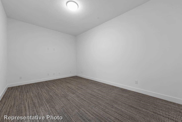 empty room with dark colored carpet and baseboards