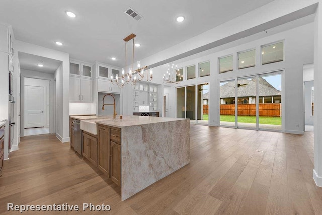 kitchen with white cabinets, visible vents, a sink, light stone countertops, and glass insert cabinets