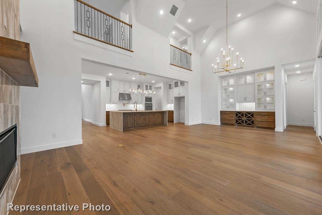 unfurnished living room featuring dark wood finished floors, visible vents, baseboards, a chandelier, and high vaulted ceiling