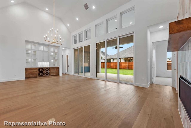 unfurnished living room with recessed lighting, light wood-style flooring, high vaulted ceiling, and a chandelier