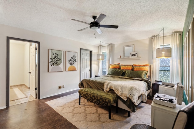 bedroom with a textured ceiling, ensuite bathroom, baseboards, a ceiling fan, and wood finished floors