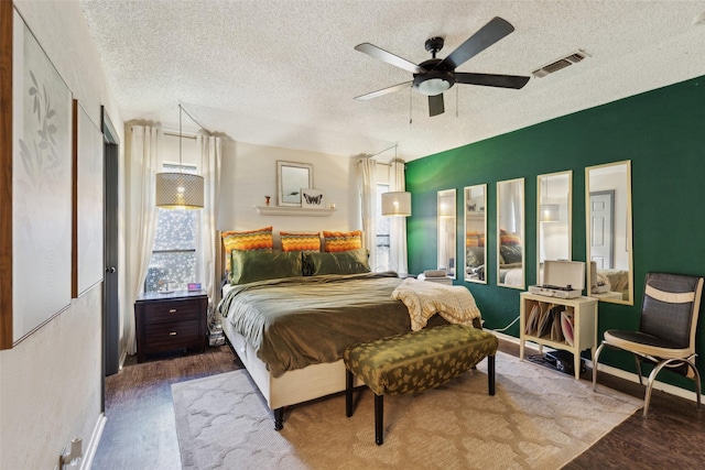 bedroom featuring baseboards, wood finished floors, a textured ceiling, and visible vents