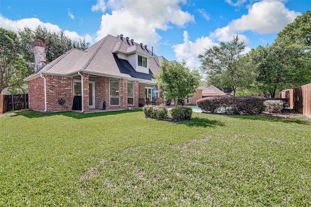 rear view of property featuring roof with shingles, a fenced backyard, a chimney, brick siding, and a yard