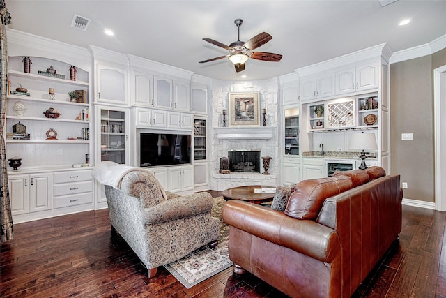 living room with a ceiling fan, a fireplace, ornamental molding, dark wood-type flooring, and visible vents