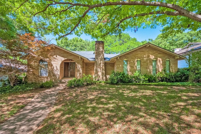 ranch-style home with brick siding, a front yard, and a chimney