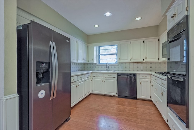 kitchen featuring decorative backsplash, light wood-type flooring, light countertops, a sink, and black appliances