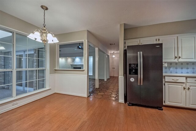 kitchen featuring pendant lighting, stainless steel refrigerator with ice dispenser, light countertops, light wood-type flooring, and white cabinets