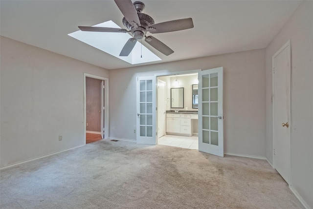 spare room with ceiling fan, french doors, light colored carpet, a skylight, and baseboards