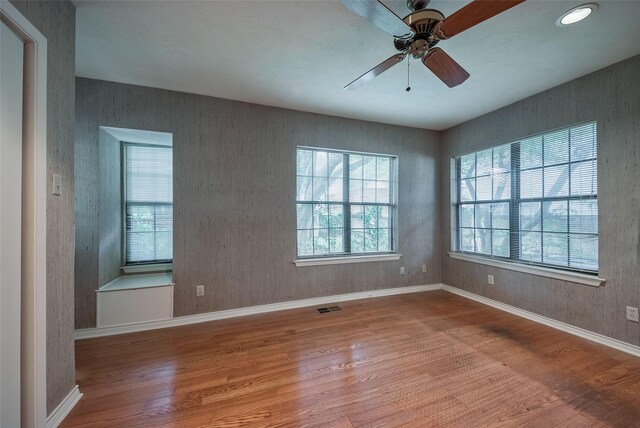 empty room with baseboards, ceiling fan, visible vents, and wood finished floors