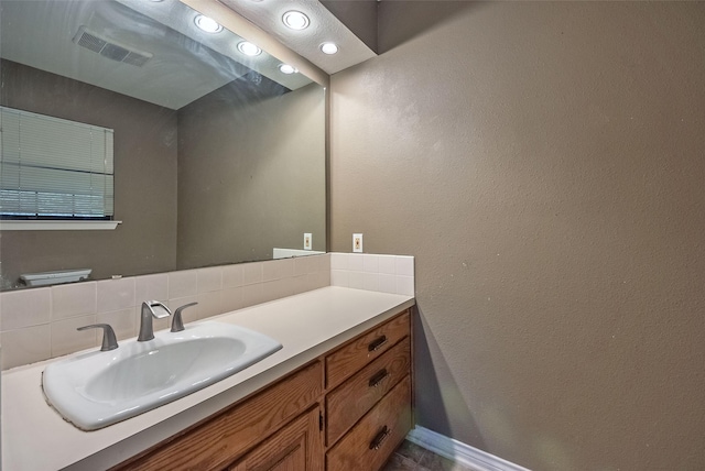bathroom featuring vanity, a textured wall, visible vents, and tasteful backsplash
