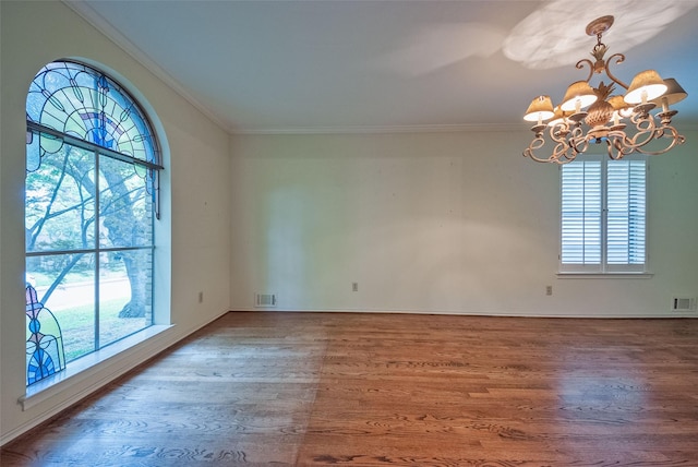 unfurnished room with an inviting chandelier, ornamental molding, wood finished floors, and visible vents