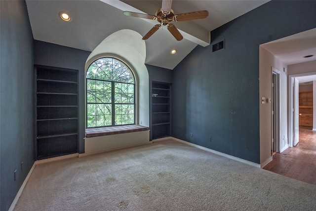 carpeted spare room with a ceiling fan, visible vents, built in features, baseboards, and vaulted ceiling with beams
