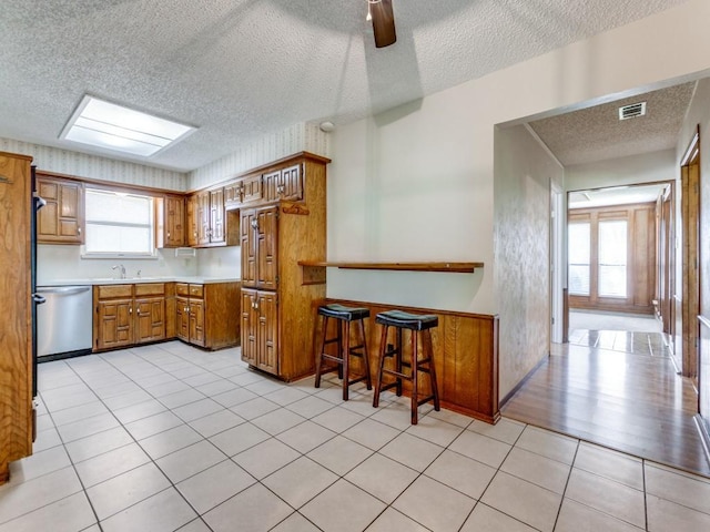 2011 Vicksburg Dr, Sachse, TX 75048 - kitchen with a textured ceiling, stainless steel dishwasher, visible vents, brown cabinets, and light countertops