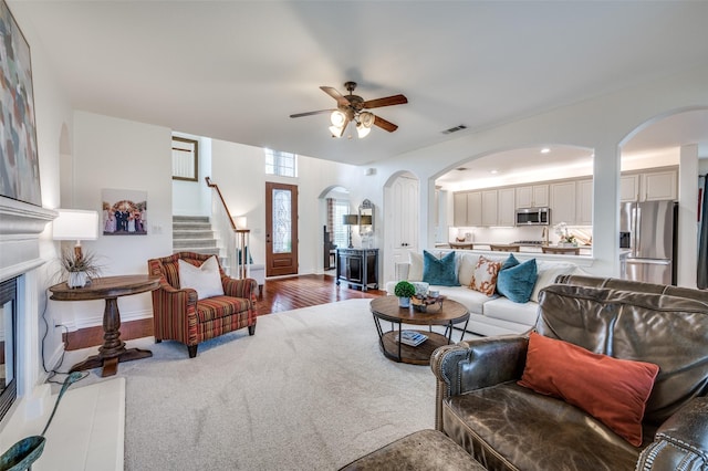 12067 Sunny St, Frisco, TX 75033 - carpeted living area featuring ceiling fan, arched walkways, stairs, a glass covered fireplace, and baseboards