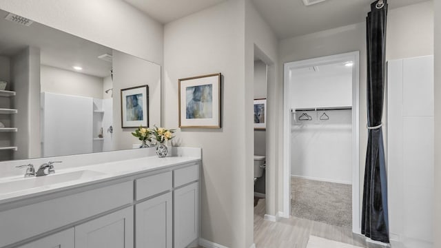 bathroom with wood finished floors, a walk in closet, vanity, toilet, and visible vents